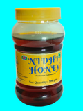 A 500g plastic jar of Nidhi Honey with a yellow lid and yellow label, filled with dark amber honey, shown against a plain white background.