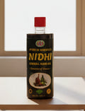 A 500 ml bottle of Ayur M Herbals Nidhi Herbal Hair Oil. The bottle is dark green with a bright red cap, and the label features yellow text and an illustration of herbal ingredients.